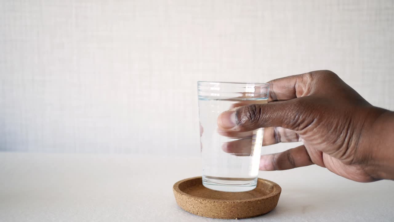 mano sosteniendo un vaso de agua en una banqueta de corcho