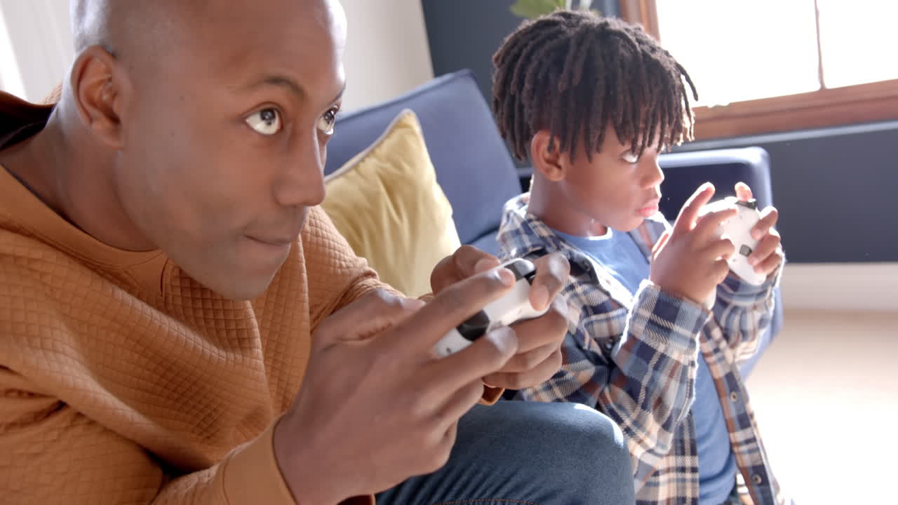 Padre e figlio afroamericani che giocano ai videogiochi a casa, al rallentatore