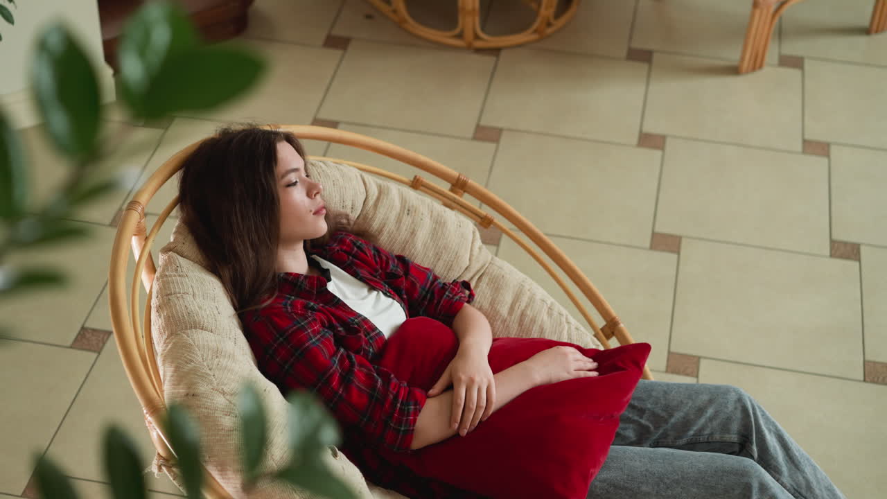 una señora reclinada en un sillón con un cojín en las manos. una mujer busca consuelo entre los rincones silenciosos del hogar perseguida por los recuerdos. un momento de vulnerabilidad