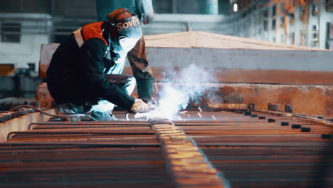 worker welding metal construction in protective mask at steel factory