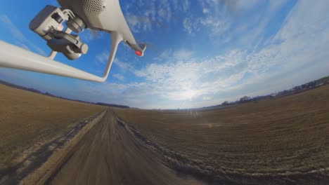 Vista-Lateral-De-Primer-Plano-Del-Dron-Quadcopter-Dji-Phantom-4-Volando-Hacia-Atrás-Sobre-Un-Camino-Rural-De-Grava