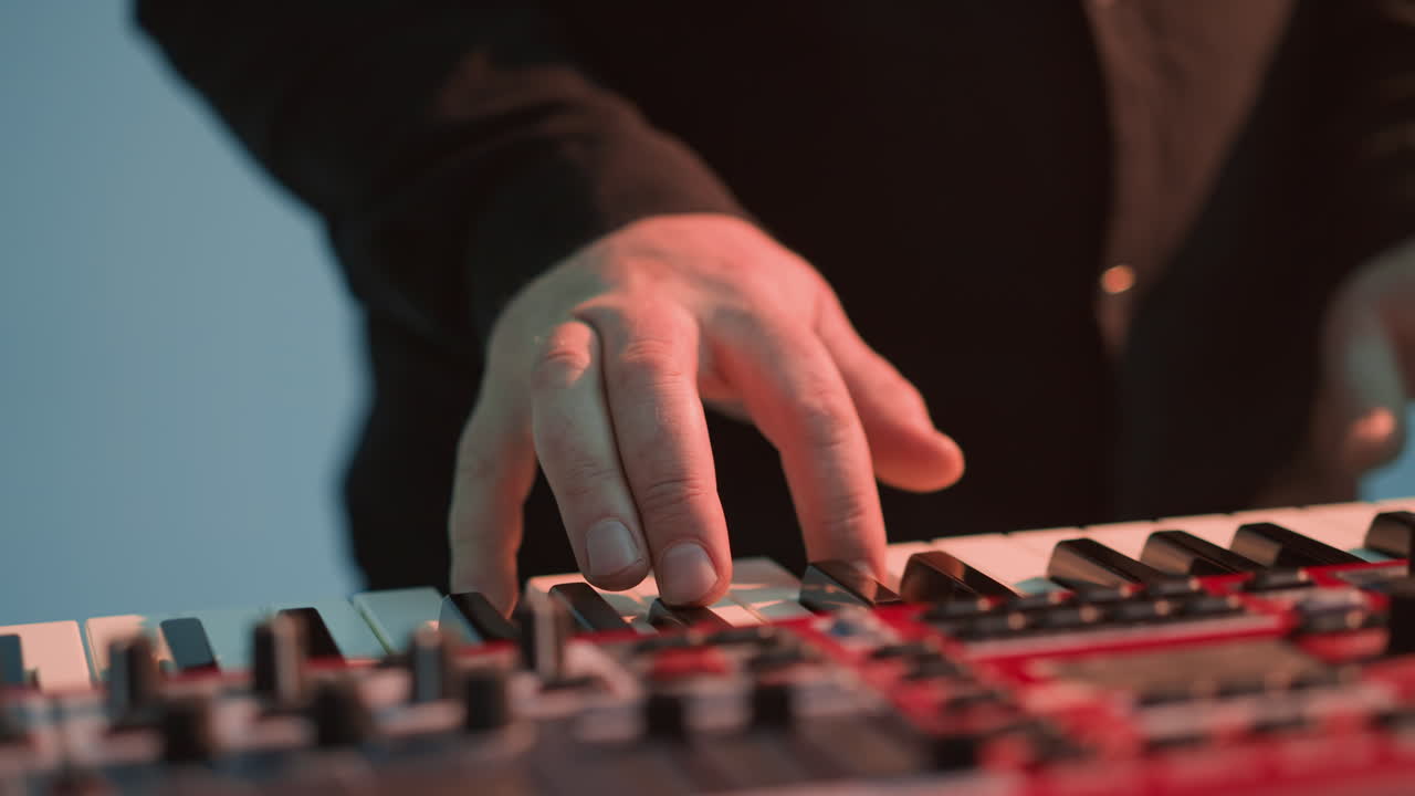 vista más cercana de un tecladista sin rostro tocando un piano sampler rojo contra un fondo azul, destacando la interacción detallada con las teclas y los controles