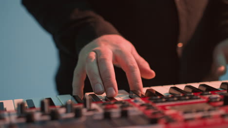 closer view of a faceless keyboardist playing a red sampler piano against a blue background,highlighting the detailed interaction with the keys and controls