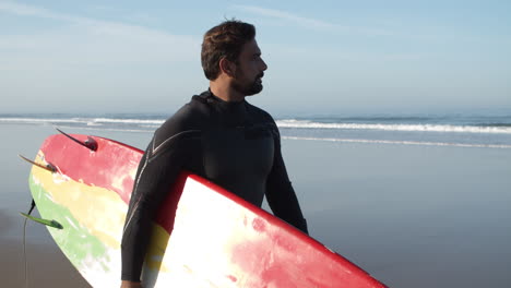 medium shot of a male surfer with artificial leg walking along beach and holding surfboard under arm 1