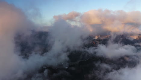 Aerial-dolly-between-wispy-mystical-clouds-reflecting-orange-sunset-light-above-mountains