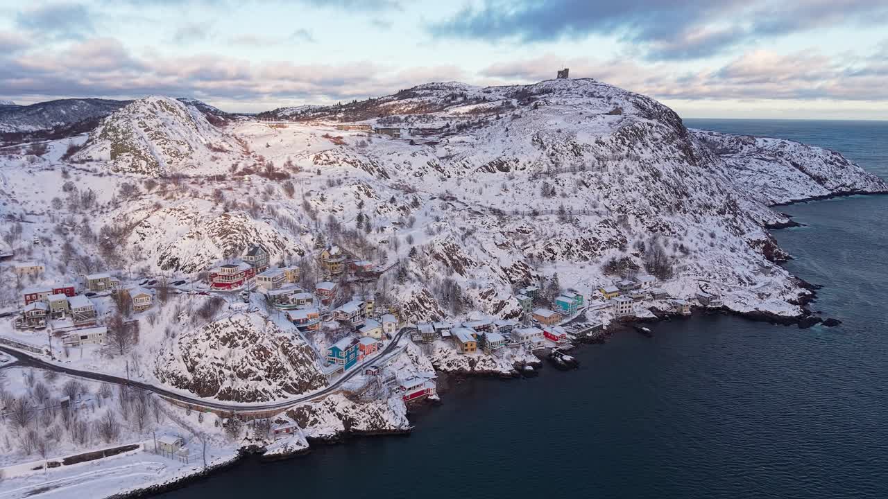 Solstråler som bryter gjennom skyene over en snødekt åsside og kystlinje, og lyser opp det robuste vinterlandskapet