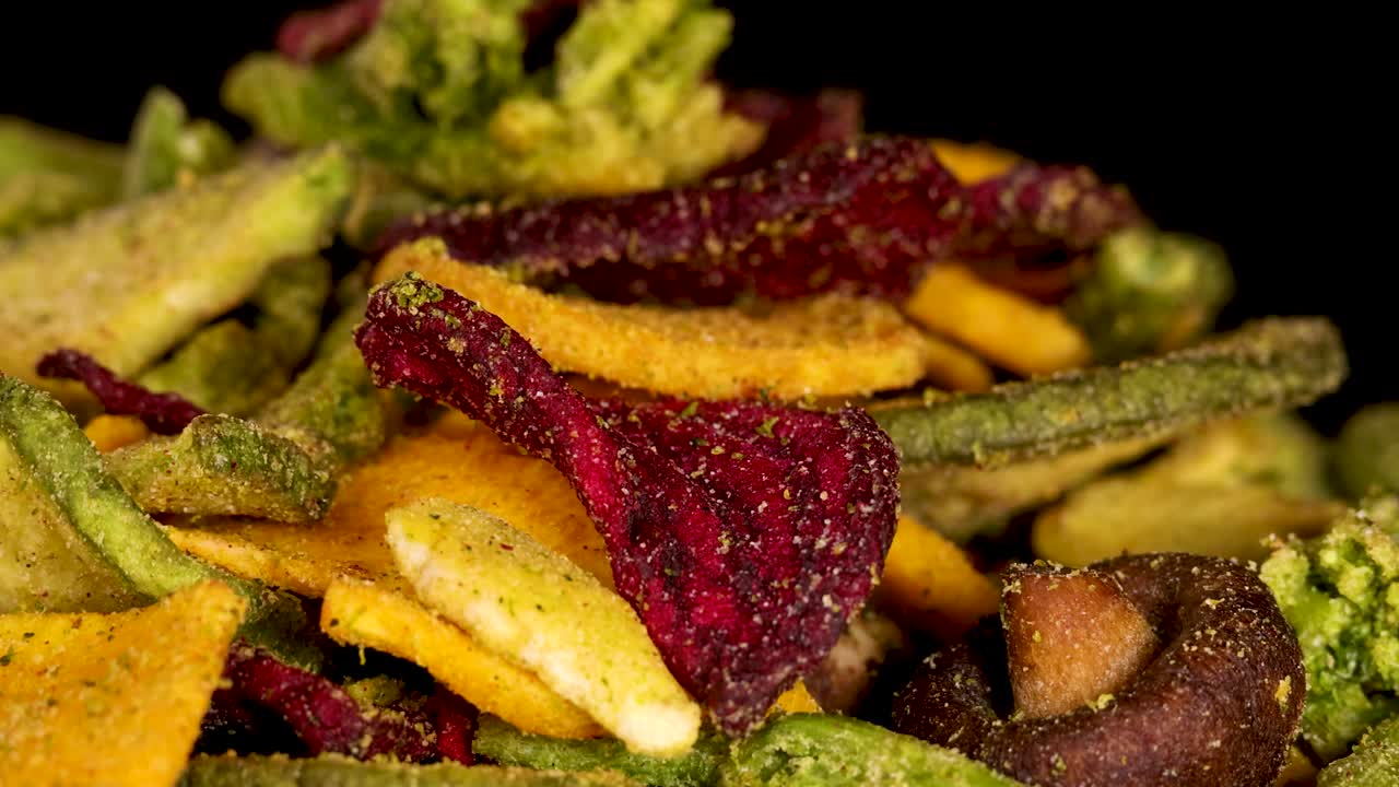 Colorful dried vegetable chips rotate slowly under bright studio lighting, highlighting crunchy textures and details