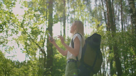 a traveler in the forest with a backpack walks along the path and looks at the mobile phone screen