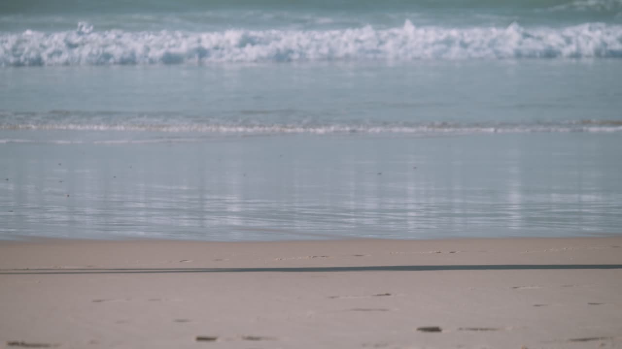 A mans legs walking barefoot along the coastline with the ocean waves behind