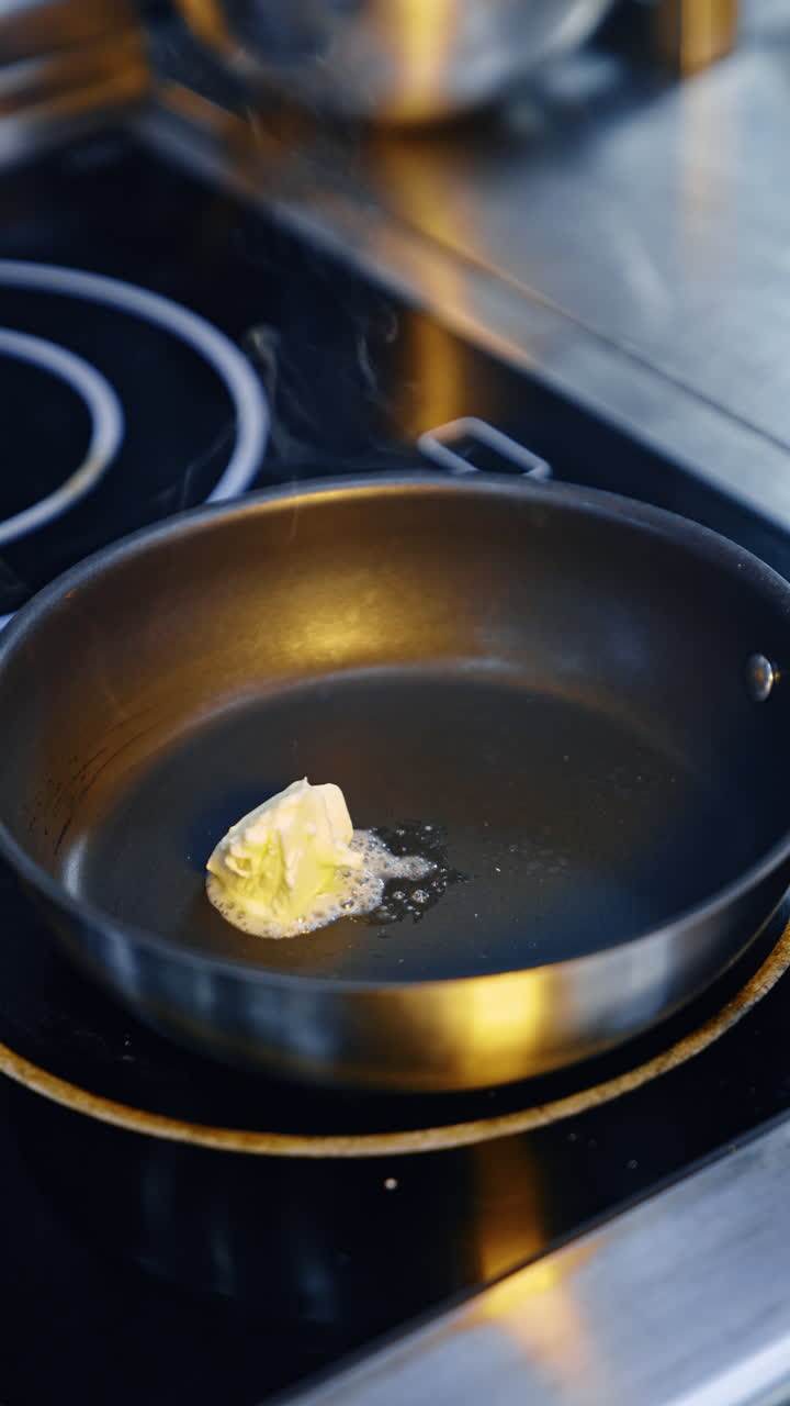 Chef puts some butter on the hot frying pan. Piece of butter starts to melt and sizzle. Vertical video.