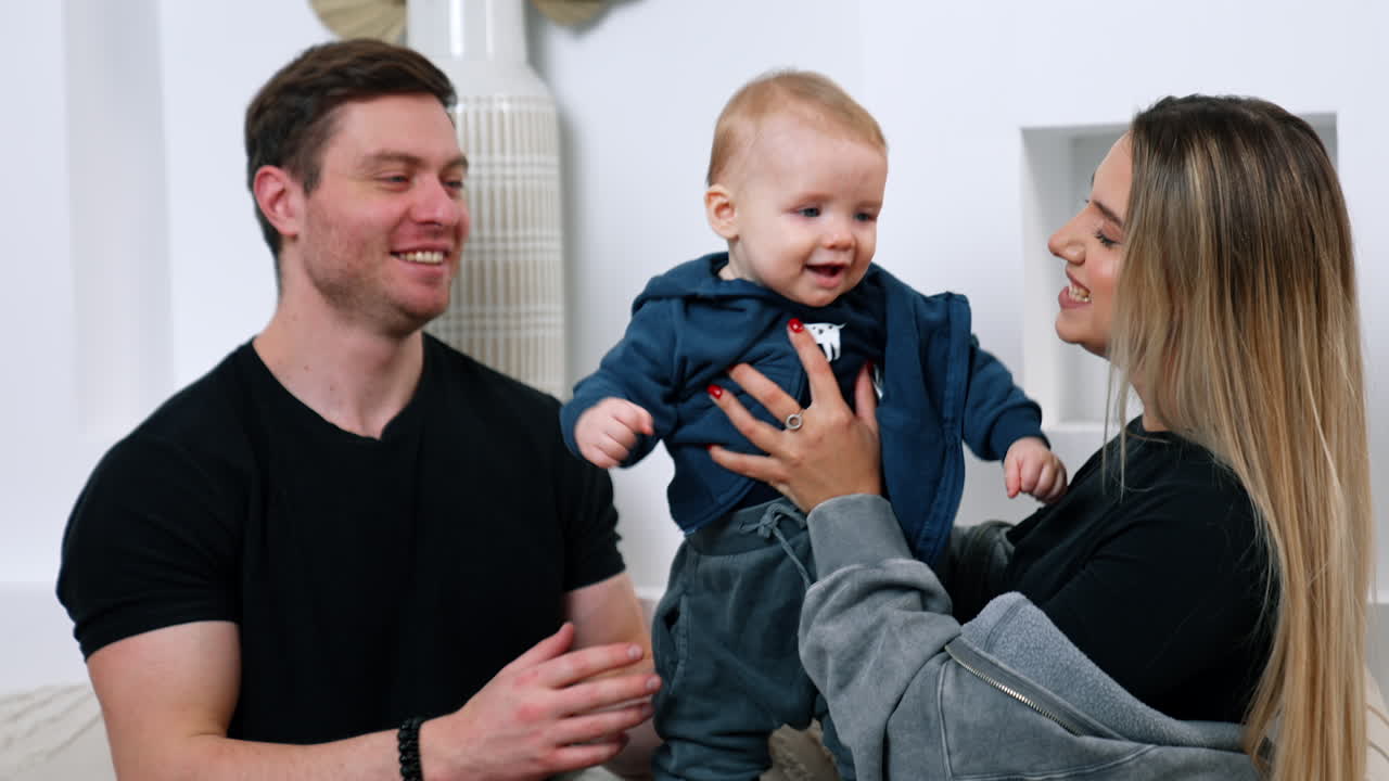 Mom and dad hold their adorable baby. Loving parents kiss the infant and kid dislikes it.