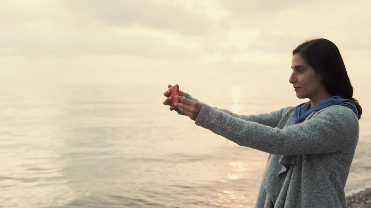 해가 지는 해변에서 셀피를 찍는 여자