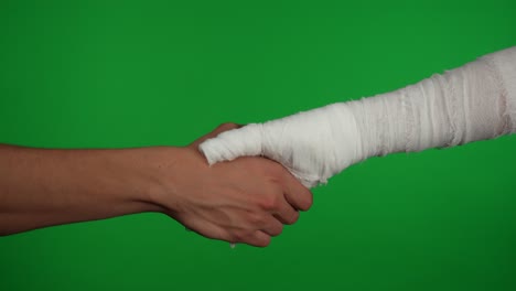handshake between a bandaged hand and an uninjured hand on green screen