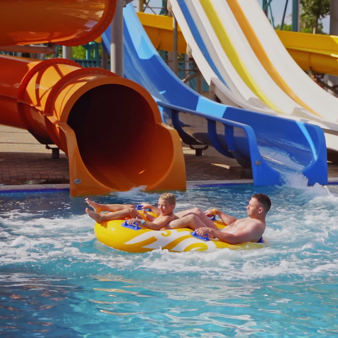 Father and son sliding from colorful pipe in the water park. Many slides in blue swimming pool in summer aquapark. Outdoor waterpark in amusement park. Joyful family vacation.