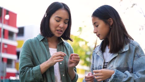 two young japanese girls looking their nails and talking about manicure while standing outdoors in the street 1