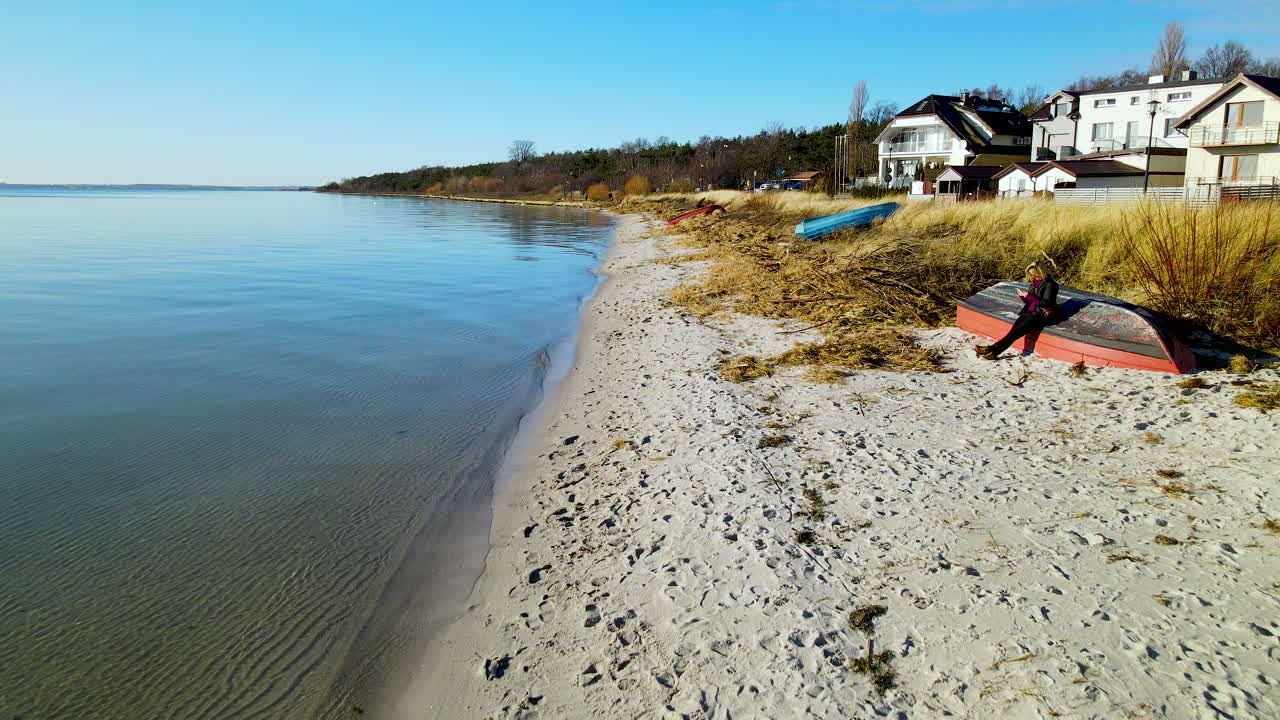 Person sidder på en omvendt båd ved strandkanten.