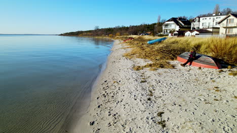 Person,-Die-In-Einem-Umgedrehten-Boot-Am-Ufer-Des-Strandes-Sitzt