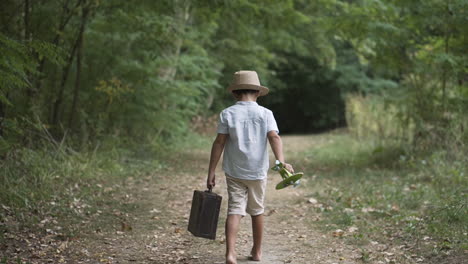 boy walking in the forest in vintage clothes carrying a suitcase and a toy plane