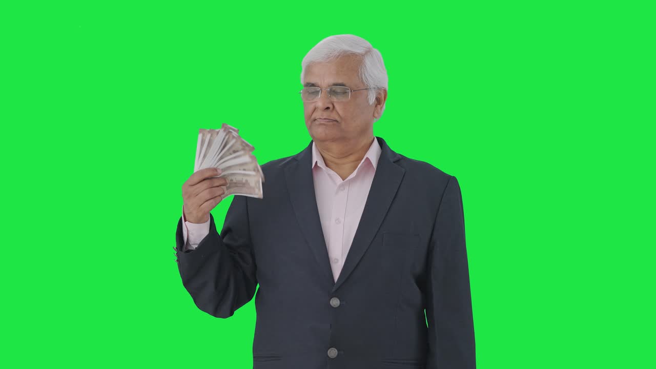 Confident Indian senior manager using money as fan Green screen