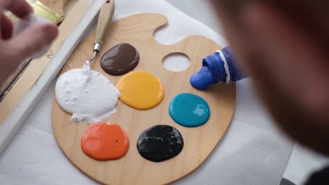 medium closeup shot of a modern artist pouring blue acrylic paint on a palette - medium close-up shot of a modern artist pouring blue acrylic paint on a palette to mix it with other colors. start drawing a picture