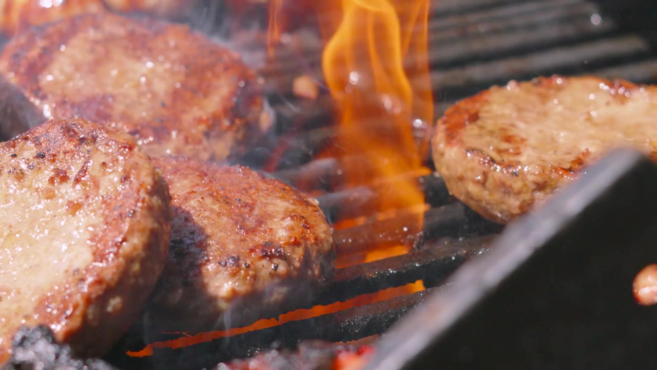 BBQ estivo con succoso hamburger di manzo spostato su una griglia fiammeggiante, con fiamme vive che cuociono carne succulenta