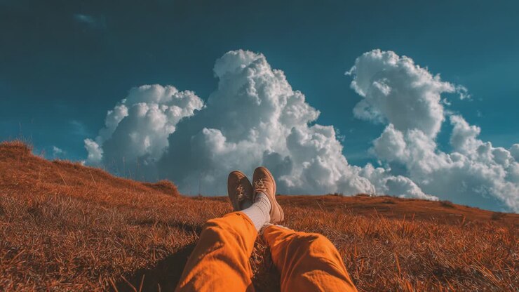Uma fuga serena: apreciando a paisagem de tirar o fôlego com nuvens do conforto de um prado ensolarado enquanto relaxa na grama macia vestindo calças laranja vibrantes