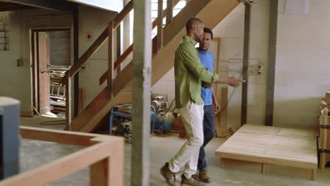 african american coworkers descending stairs to shop, pointing at bench, assembling using tablet