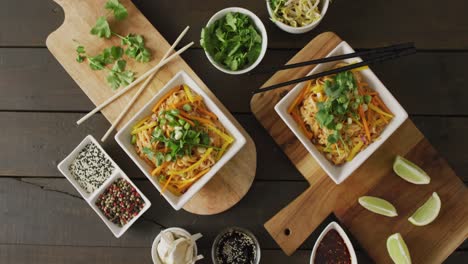 composition of bowls with pad thai, vegetables, sauces and spices on wooden background