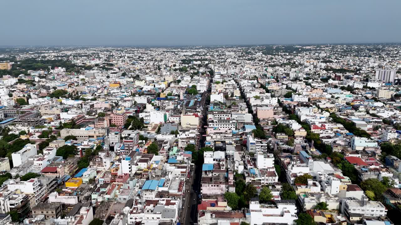 This aerial footage presents a wide, high-angle view of densely populated city. A long, straight road acts as a central axis, with countless low-rise buildings extending to the horizon on both sides