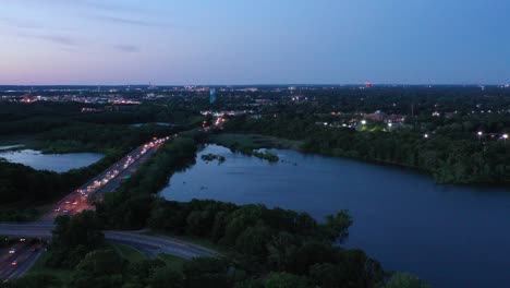 a-slow-aerial-drone-flight-towards-a-lake-with-traffic-on-the-highway-on-the-left,-then-a-slow-tilt-down-to-the-trees-and-water