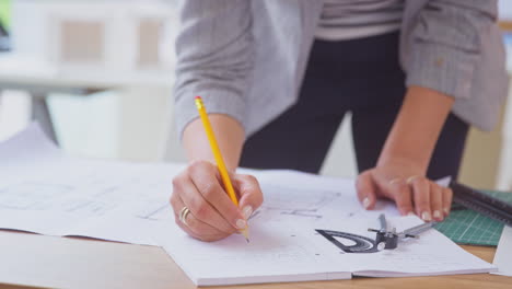 Nahaufnahme-Einer-Architektin-Im-Büro,-Die-Am-Schreibtisch-Steht-Und-An-Plänen-Für-Ein-Neues-Gebäude-Arbeitet