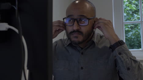 trabajador de oficina masculino caminando al escritorio y sentado, insertando auriculares