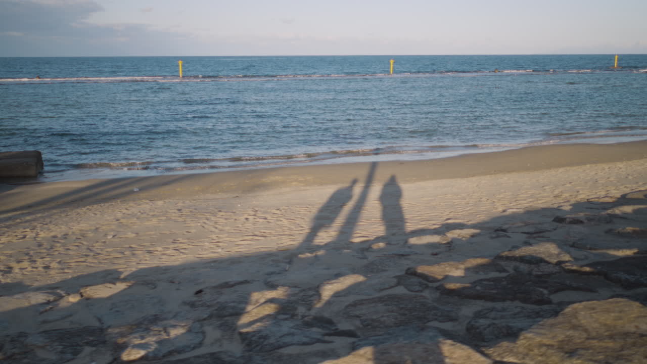 Shadow silhouette of two people walking along the coastline of Amaharashi at sunset