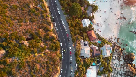 Vista-De-Arriba-Hacia-Abajo-De-Los-Autos-Que-Conducen-En-Clifton-Beach-Road-Durante-La-Puesta-De-Sol-En-Ciudad-Del-Cabo,-Antena