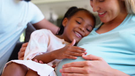 family with daughter cuddling pregnant mother at home together