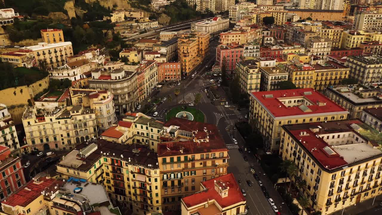 Ripresa aerea dall'alto che mostra il traffico su una rotonda nel centro storico di Napoli durante un tramonto dorato.