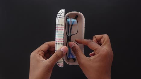 manos sosteniendo un par de gafas y un caso a cuadros