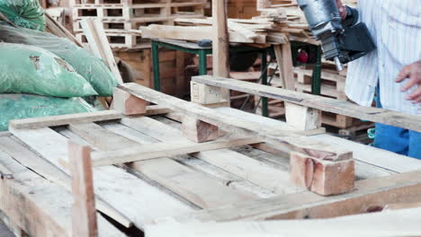 hombre en un almacén usando una pistola de clavos para paletas de madera