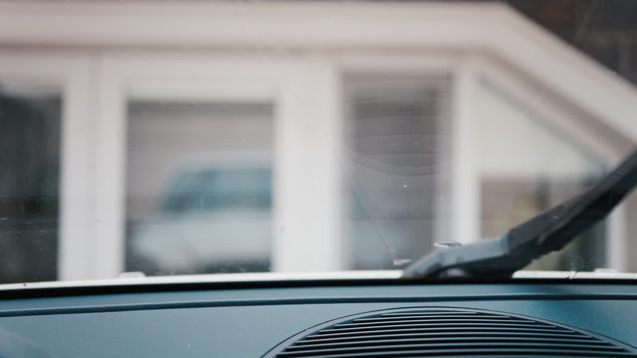 Interior perspective of windshield wipers in motion, cleaning raindrops from a car's window