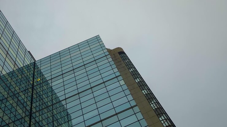 Rascacielos de gran altura con paneles de ventanas cubriendo la fachada del edificio, con cielo nublado de fondo. Concepto de finanzas, negocios 4K.