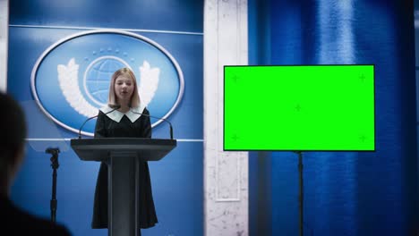 young girl activist delivering an emotional and powerful speech at press conference in government building with green screen mock up on display. child speaking to congress at summit meeting.