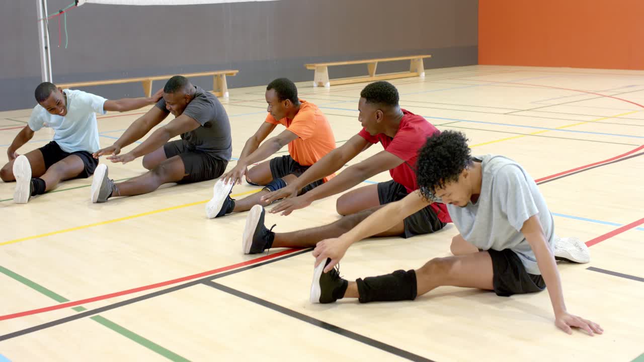 Diverse männliche Athleten hören Traineranweisung, lehnen sich vor, dehnen sich am Netzpfosten, Trainer korrigiert die Haltung.
