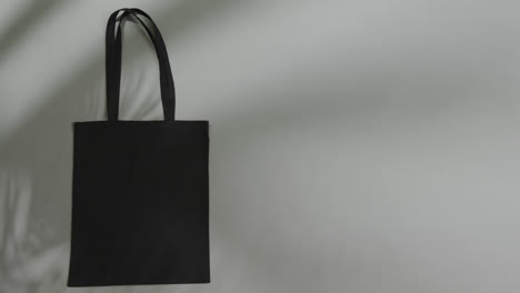 leaf shadow moving over black bag on grey background, copy space, slow motion