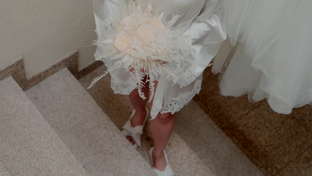 Sposa che scende le scale con un bouquet di fiori dai colori tenui, a fuoco morbido