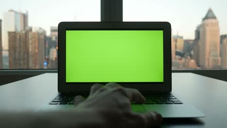 computadora con pantalla verde en un edificio de oficinas moderno con fondo de paisaje urbano.