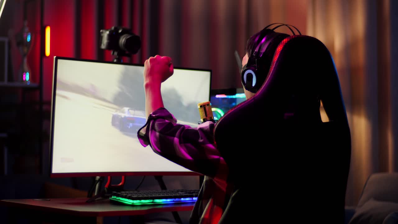 아시안 소년 스트리머의 뒷모습, 소리치는 골, 개인 컴퓨터에서 네트워크를 통해 우승 자동차 레이싱 게임을 축하하는, 라이브 스트리밍 비디오 게임, rgb led 스트립 라이트에 의해 조명 된 책상