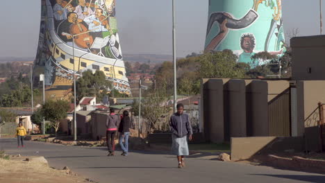 sowetan people walking in street with houses and the landmark soweto cooling towers in the background.