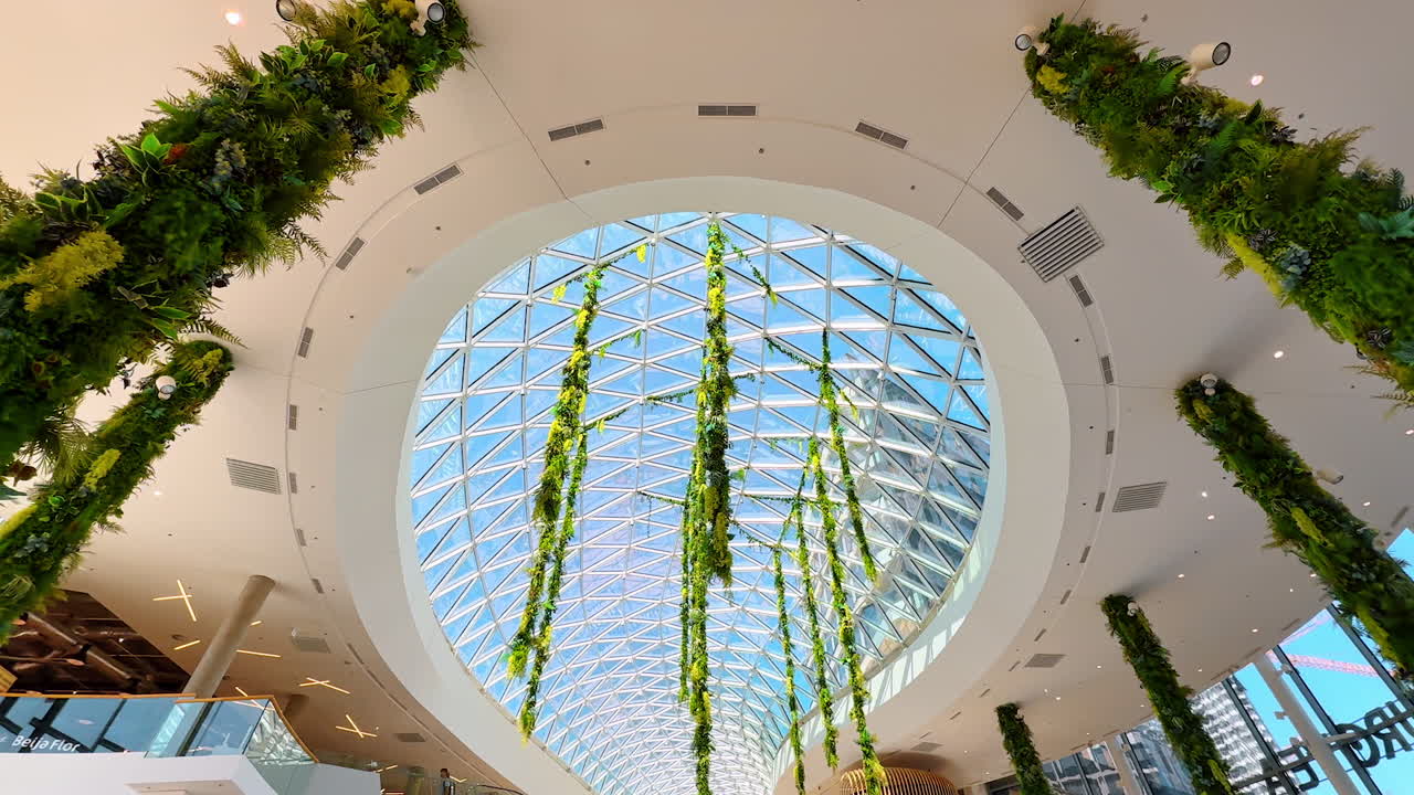 Greenery in modern design. A spacious interior with tall columns, vibrant plants, and natural light streaming through a glass roof