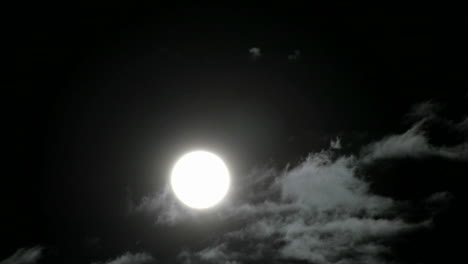 a bright full moon rises above swiftly moving clouds in the night sky