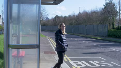 Blonde-young-woman-waits-for-the-bus-at-a-bus-stop-sitting